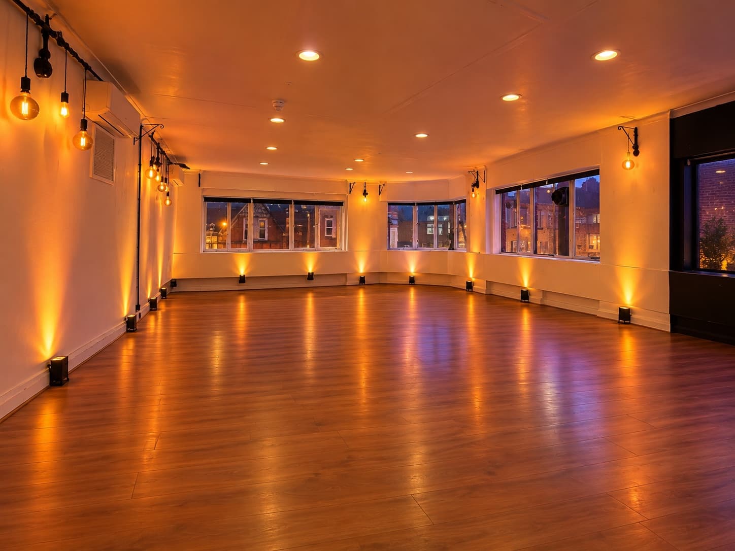 The Old Black Bar — polished wooden floor, warm uplighting along the walls, windows over Coldharbour Lane at dusk