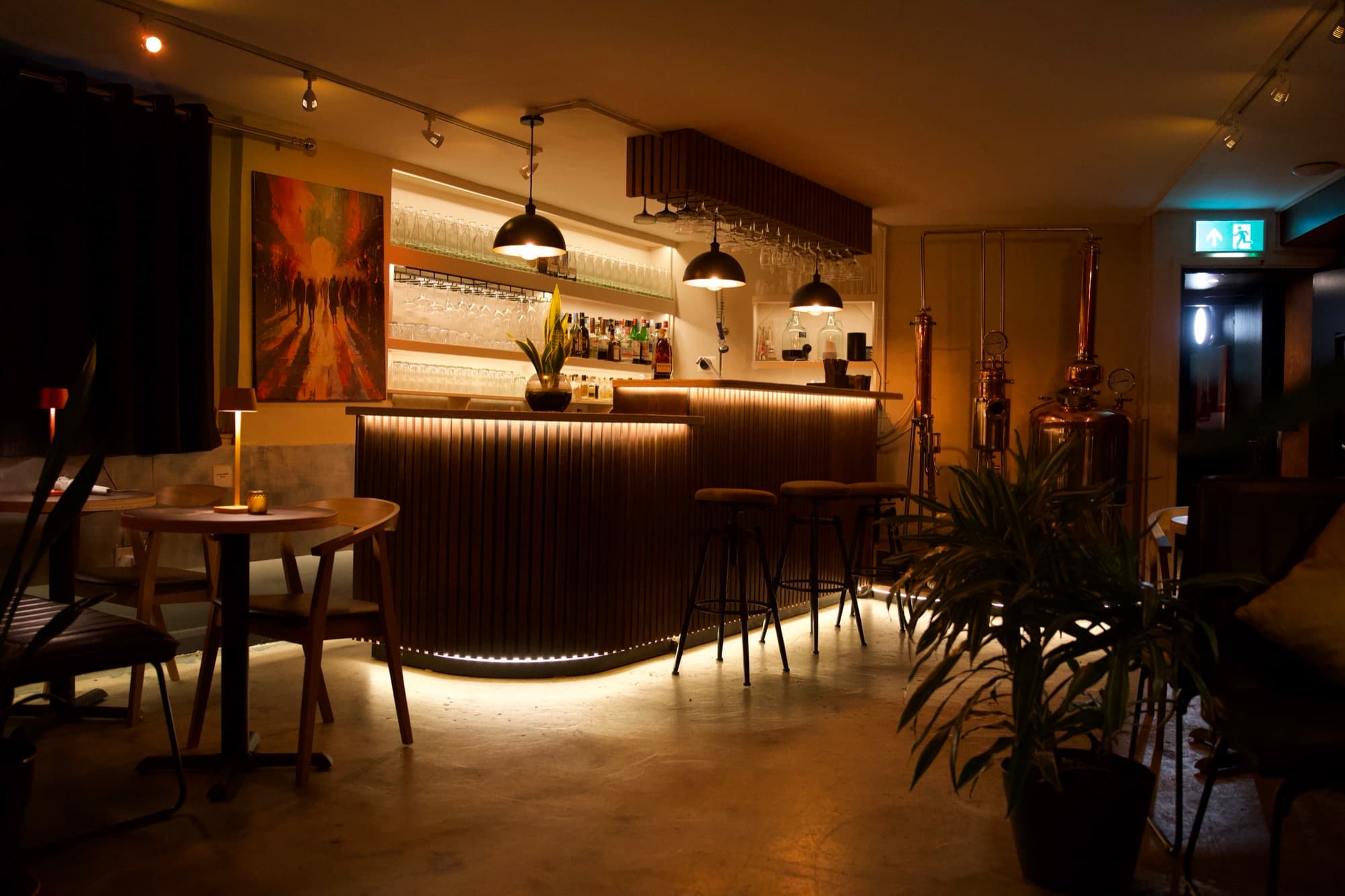 The BCC Bar after dark — the curved timber bar under pendant lamps, the copper still lit behind it