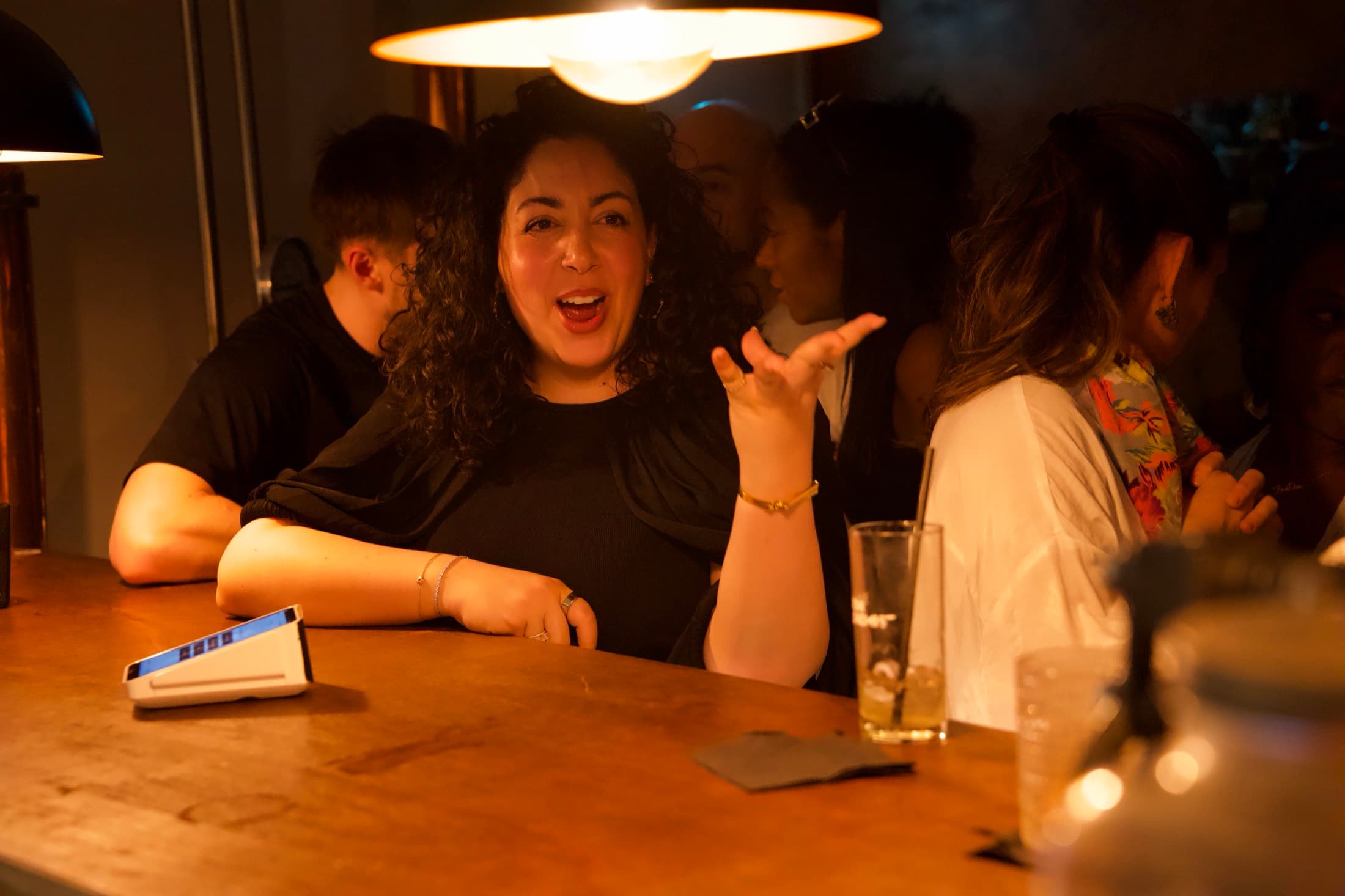 A guest laughing mid-story at the timber bar under a pendant lamp