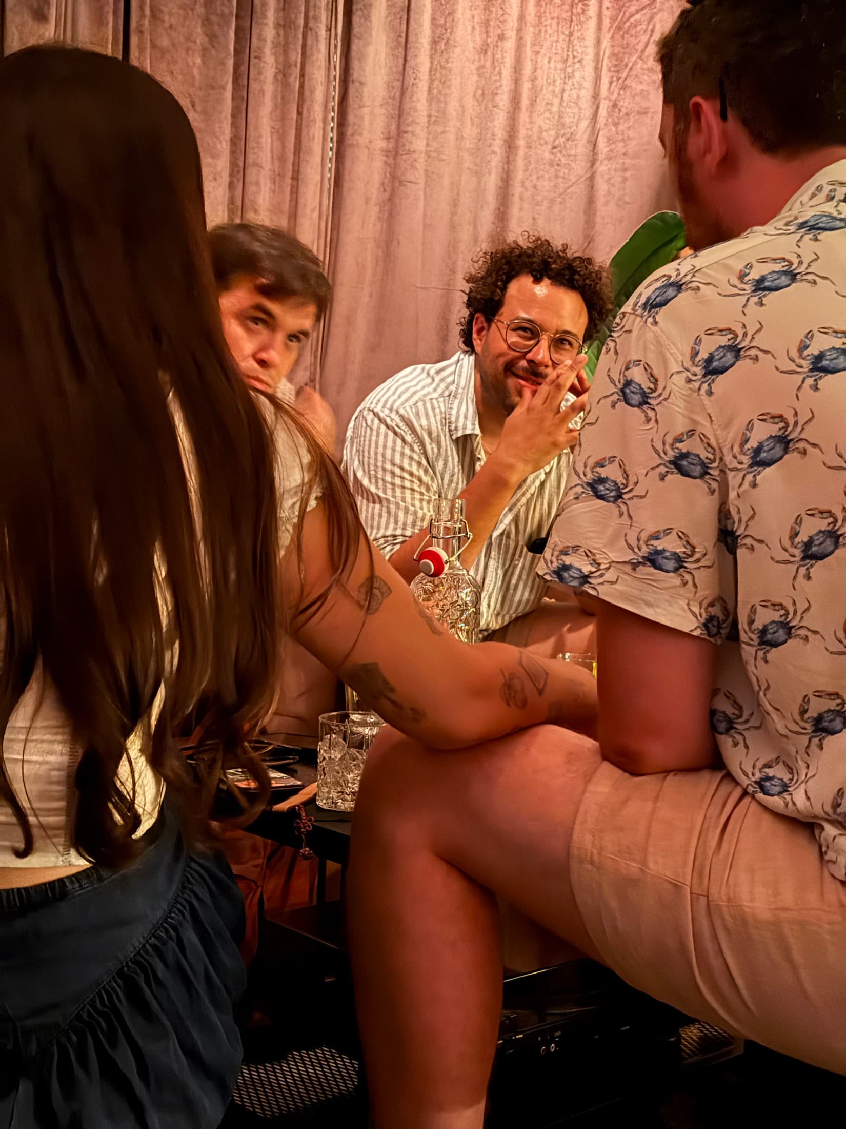 A booth against the curtained wall — guests around a low table with a bottle of house rum