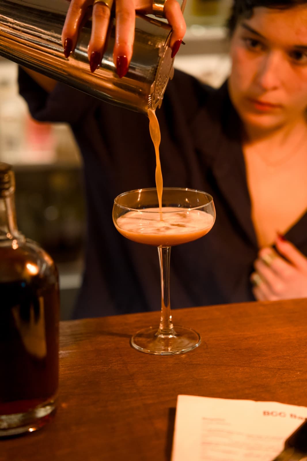 A bartender pouring a cocktail from the shaker into a coupe