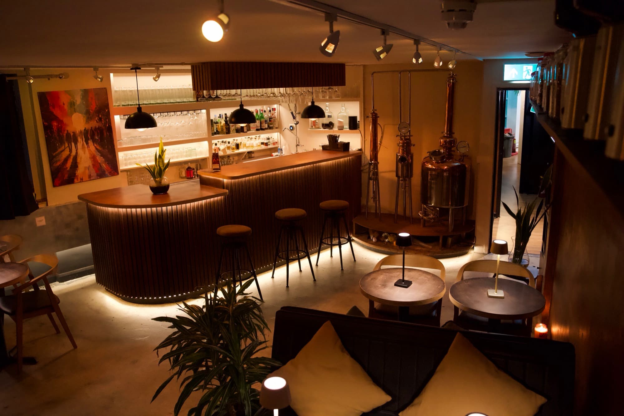 The BCC bar room — curved timber bar with underglow, the copper still behind, banquettes and stools