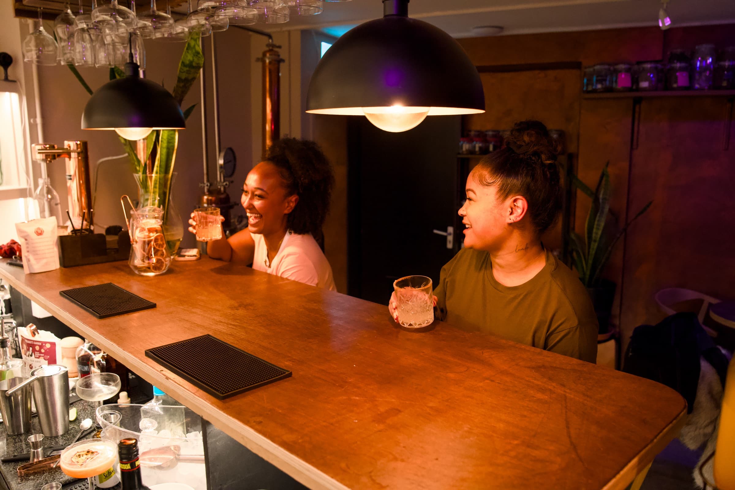 Two guests laughing over glasses at the BCC Distillery bar in Brixton Village