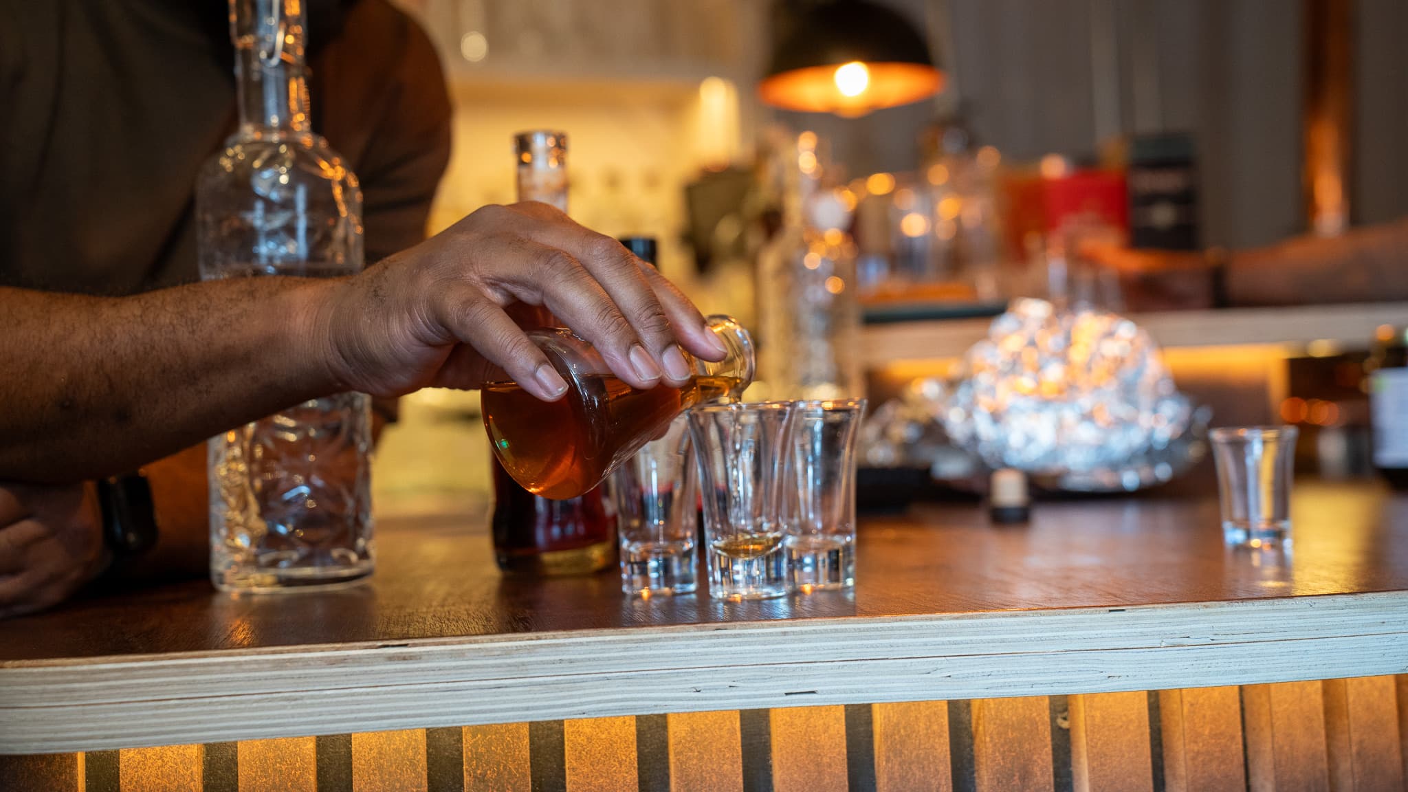 The host pouring rum from a flask into a row of tasting glasses on the bar